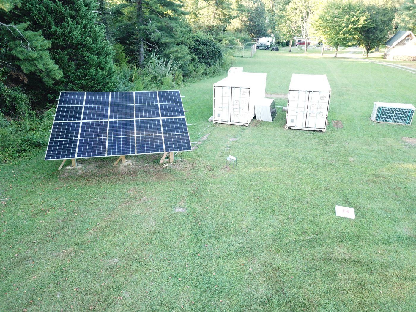 Aerial view of the Gloucester proving ground: ground-mounted solar array, two ISO containers, sensor station and landing pad on a grass field