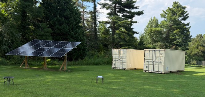 Eclipse Prototype 1 at Gloucester: ground-mounted solar array, two ISO containers, and environmental sensor stations on a grass field